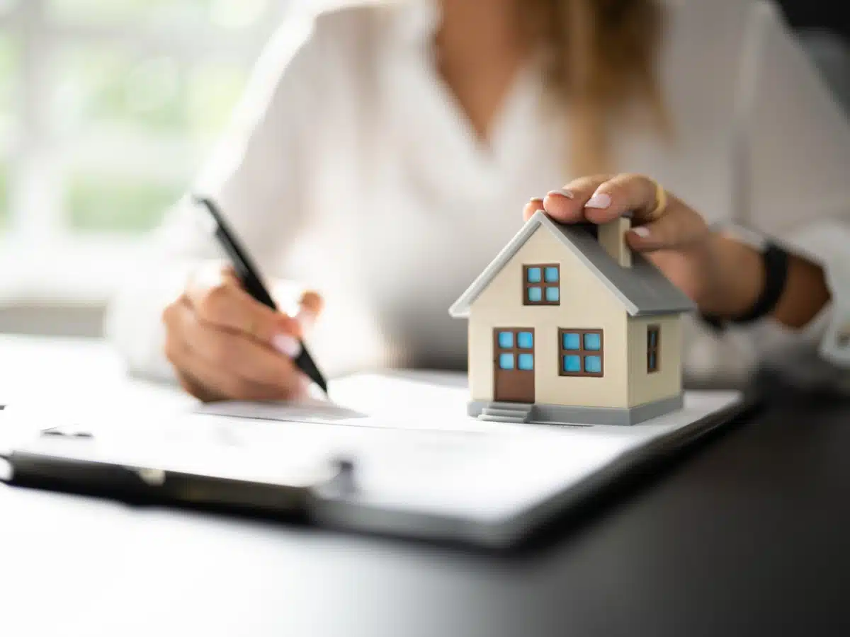 Homebuyer signing paperwork with a small house model, illustrating how to buy a home in Denver with local guidance.