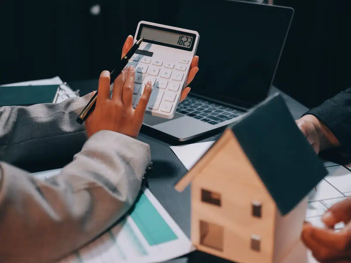 Denver real estate agent calculating home value using a laptop, calculator, and model house.