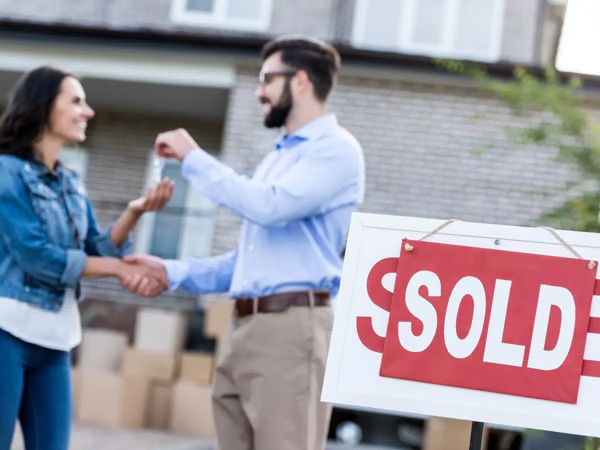 Denver real estate agent handing house keys to a happy homebuyer outside a new property.