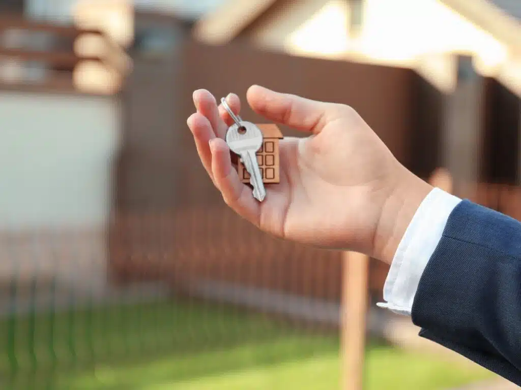 Hand holding a set of house keys with a blurred home interior in the background.