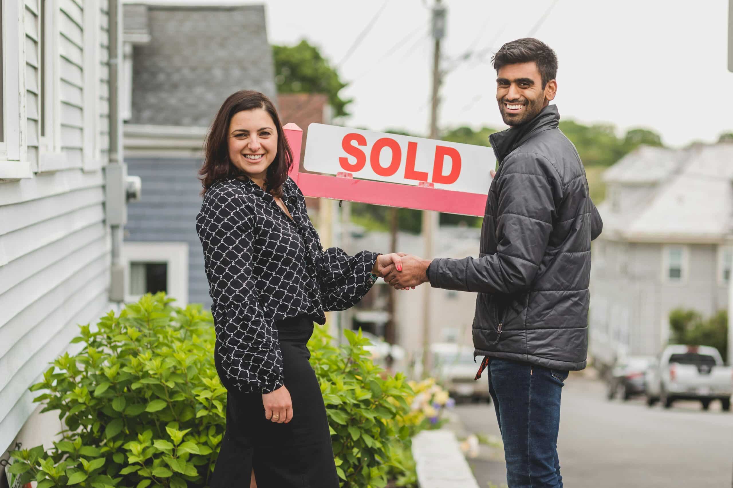 Happy homeowners holding a SOLD sign after working with a Denver real estate agent.