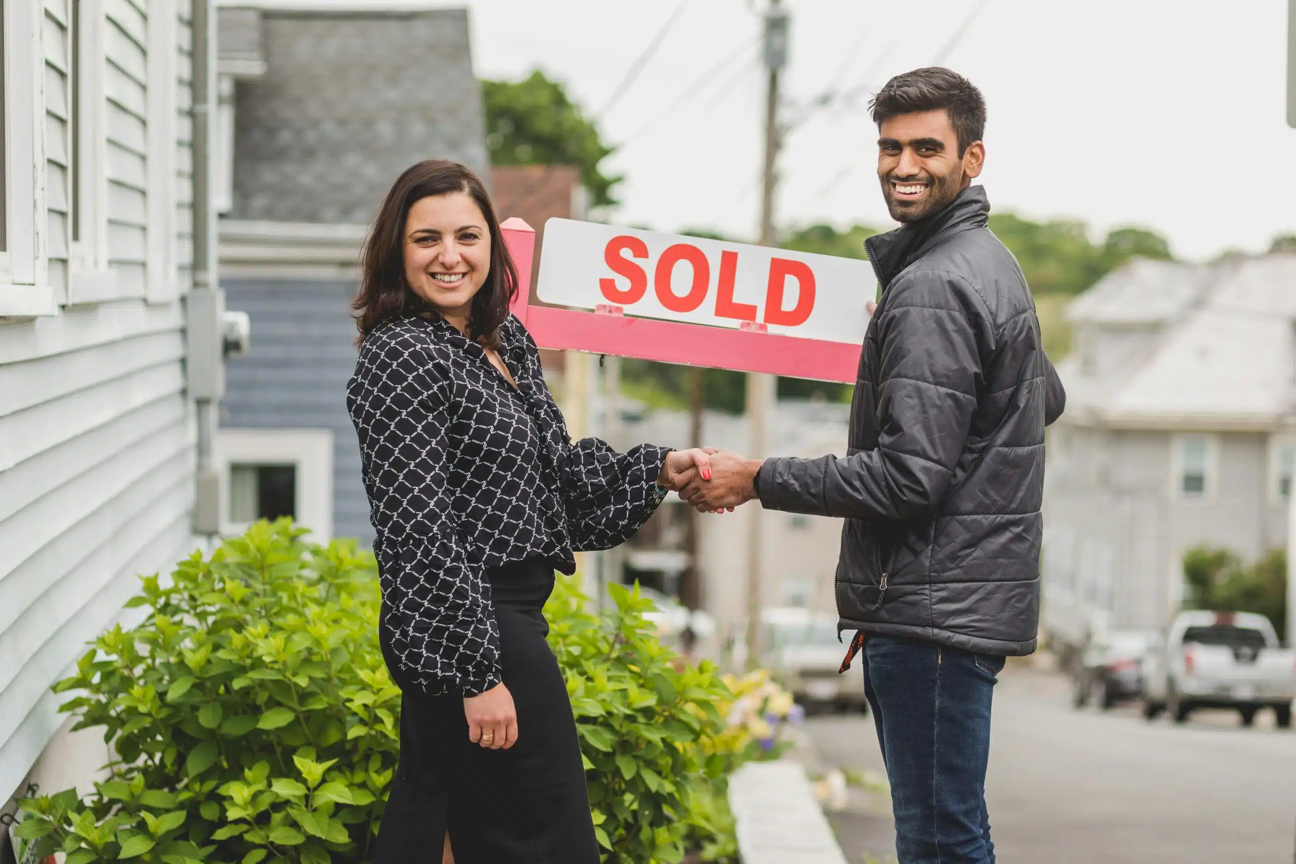 Happy homeowners holding a SOLD sign after working with a Denver real estate agent.